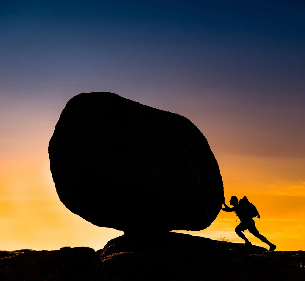 silhouette man pushing a rock at sunset